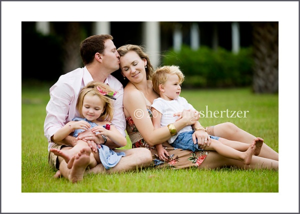 Pure family love is expressed perfectly as the father kisses mom while kids are snuggled in their laps.
